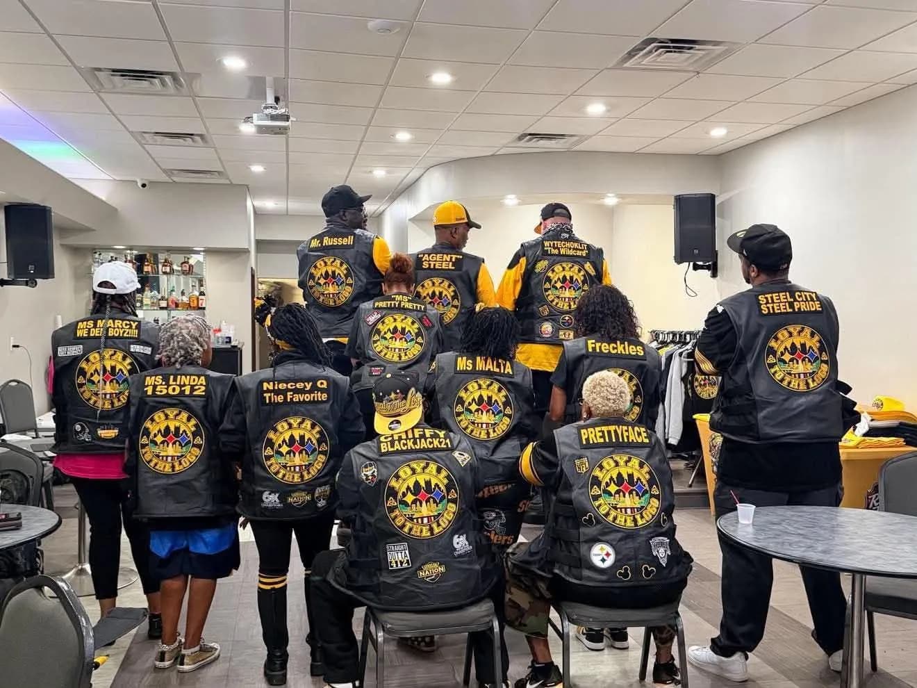 Fan group members seen from behind, each black vest with the round embroidered club emblem.