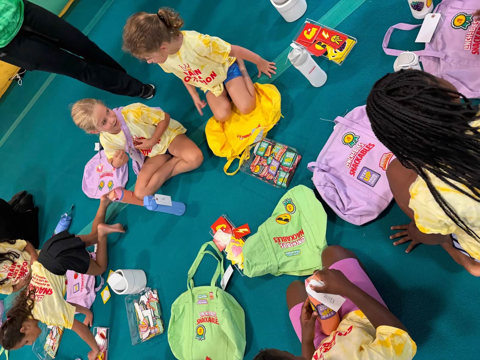 Children at a youth gymnastics camp choosing peel-and-stick patches from display trays and applying them to event tote bags
