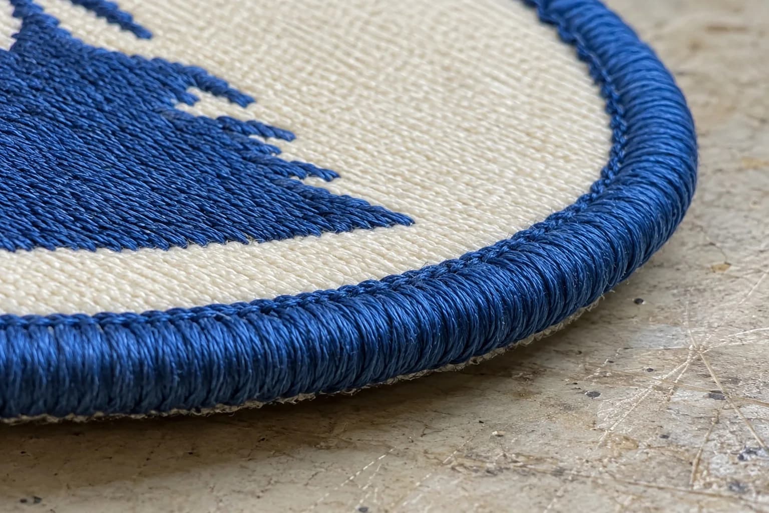 Close-up of a merrowed border: a raised, rope-like blue overlock stitch wrapped around the curved edge of an embroidered patch